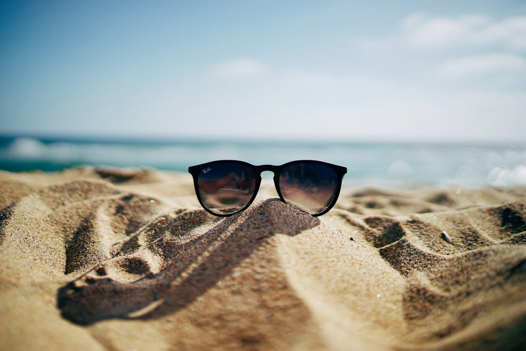 Pair of sunglasses on a pile of sand at the ocean. 